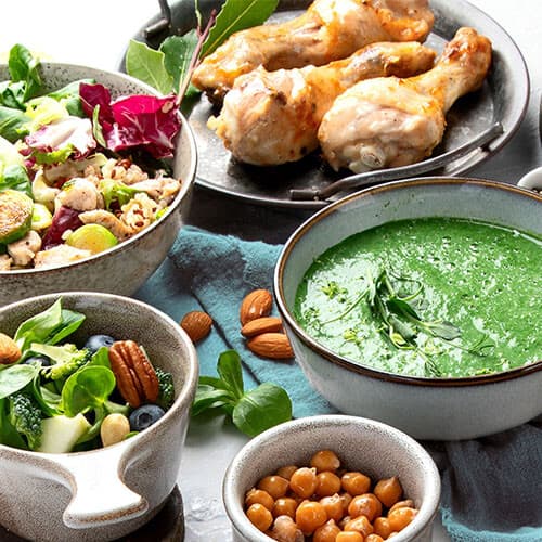Plates of salad, legumes, cream of vegetable soup and chicken.